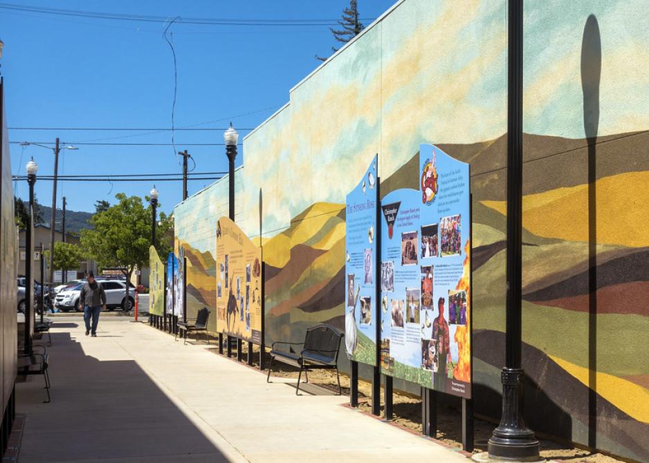 Photo of a colorful mural with a sign in front on a sunny day
